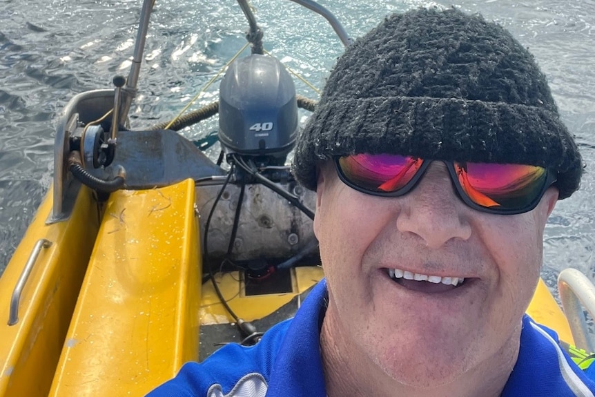 a man's selfie, he is wearing a beanie and glasses and is on the ocean