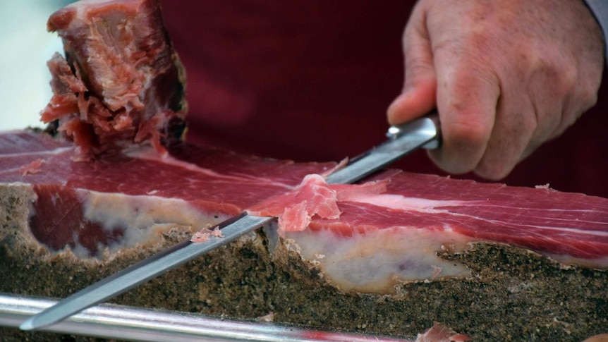 Close up of a butcher shaving thin slices of prosciutto ham.