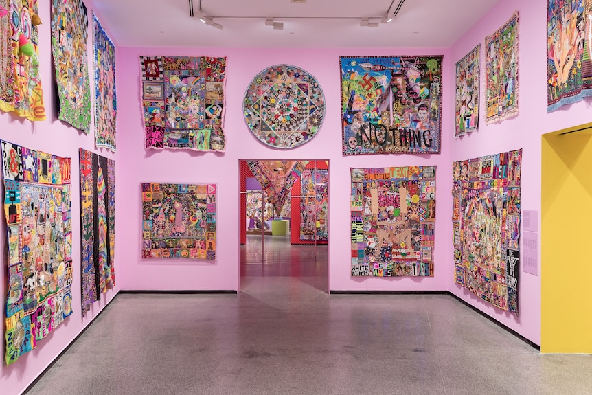 A gallery room with pink walls and colorful textile works