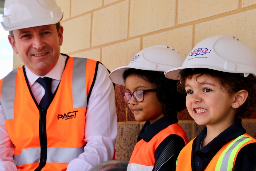 Mark McGowan and two small children wear safety helmets and high-vis vests.