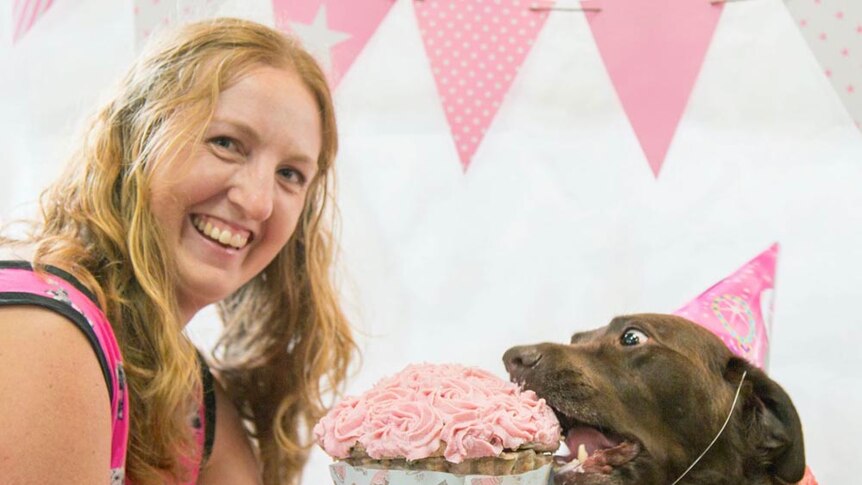 A woman sits beside a dog eating cake