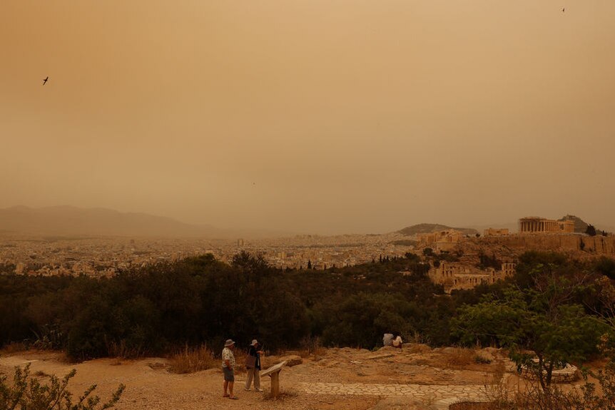 A view of the Athens cityscape with a red brown hue from a dust cloud.
