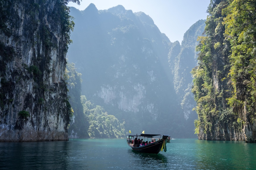 Large mountains on top of blue water with a small boat in it 