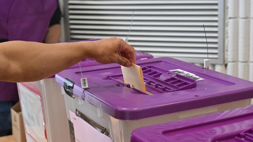 a ballot paper is dropping in a sealed ballot box with a purple lid
