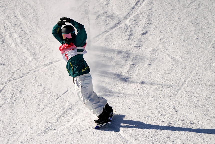An Australian Winter Olympian holds her hands to her helmet as she moves across the snow on her snowboard after a run