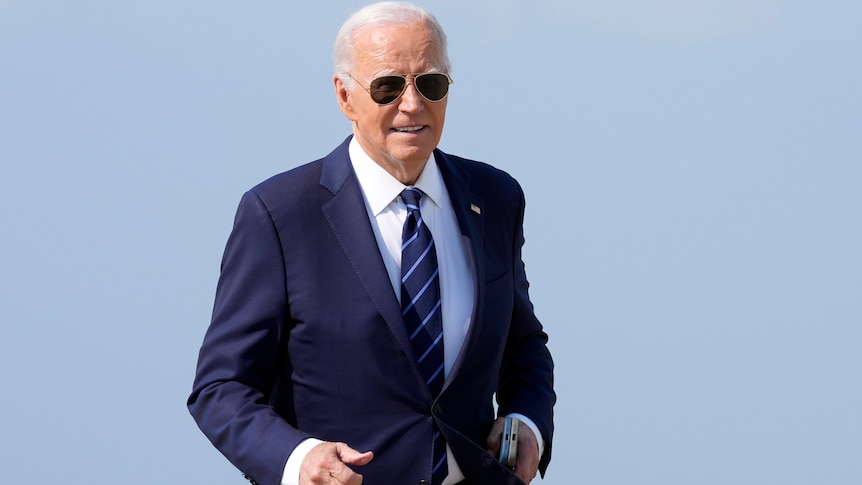 Joe Biden in suit and sunglasses walking over to reporters
