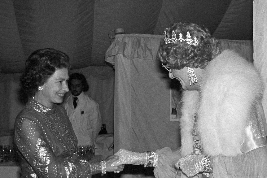 Black and white of Queen Elizabeth II shaking hands with Dame Edna in 1977.