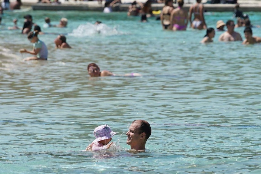 A man swims with a little girl, with other swimmers in background, at Brisbane's South Bank lagoon.