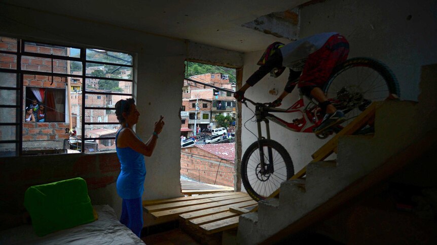 A woman photographs a downhill rider as he rides through her house during the Adrenalina Urban Bike race final.