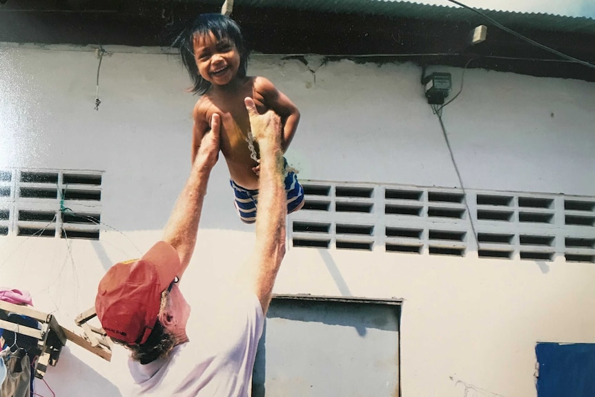 a man wearing a hat lifts up a child who is giggling