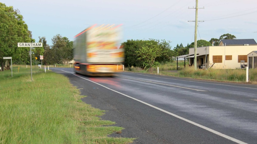 a blurred truck on the road passes a Grantham road sign