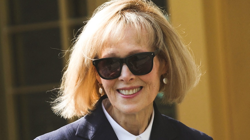 A woman with a blonde bob and wearing sunglasses smiles outside court.