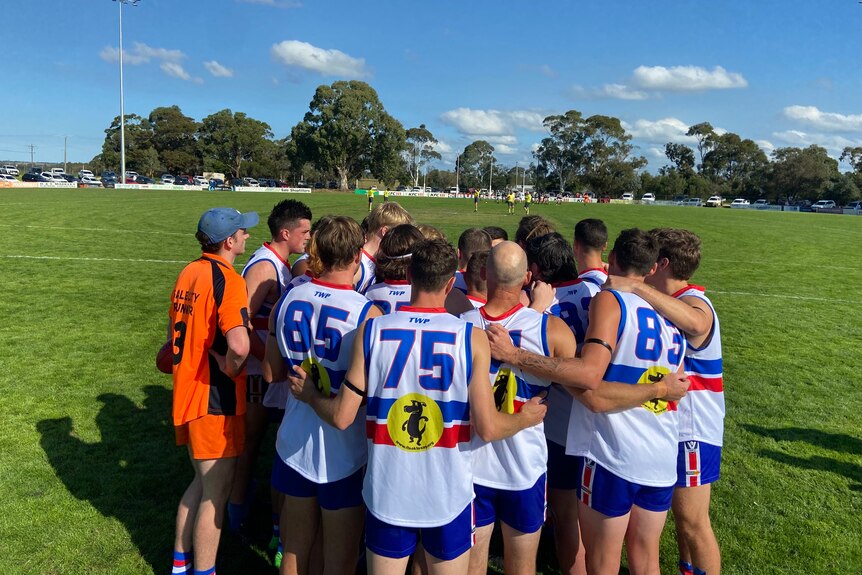 An Aussie rules team in red, white and blue guernseys stand in a huddle on a field.