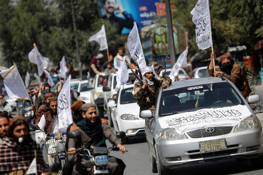 Taliban members on bikes and in cars join a celebratory convoy, holding up Taliban flags.