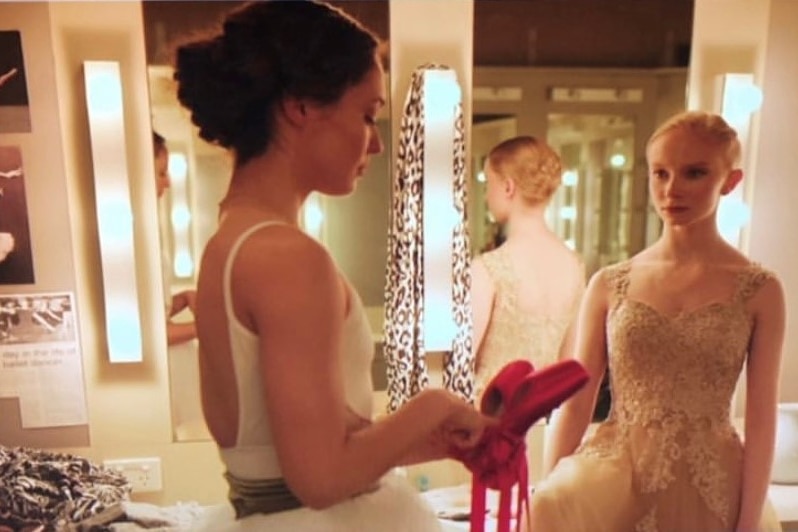 Two ballerinas talking and one holding red pointe shoes