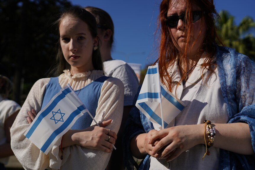 a young woman and a lady hold israeli flags at a rally in support of israel in brisbane