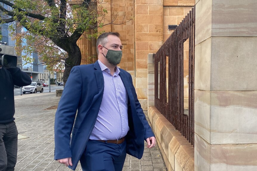 A man in a blue suit wearing a face mask walking