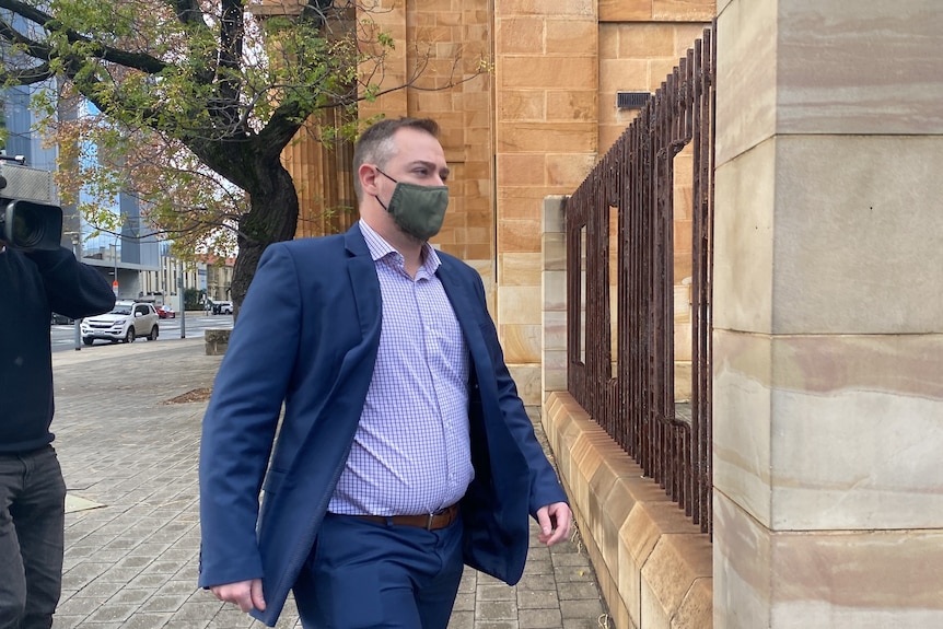 A man in a blue suit wearing a face mask walking