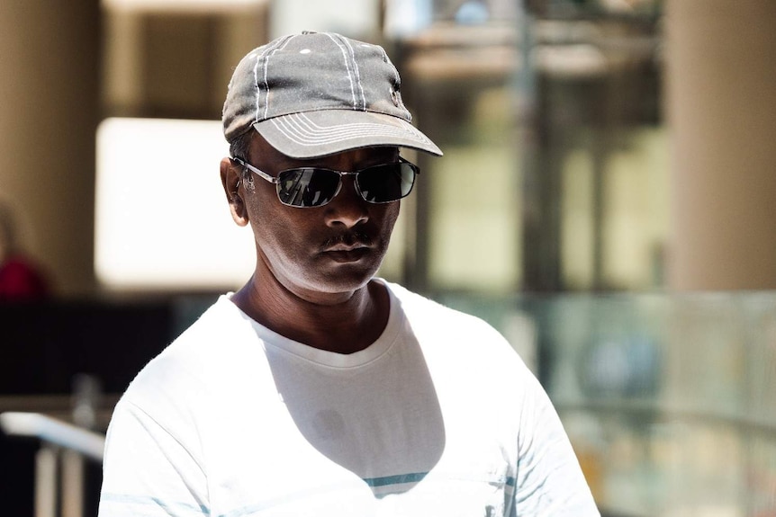 Ootamcoomar Dhurumsing wearing a white shirt, worn out baseball cap and sunglasses.