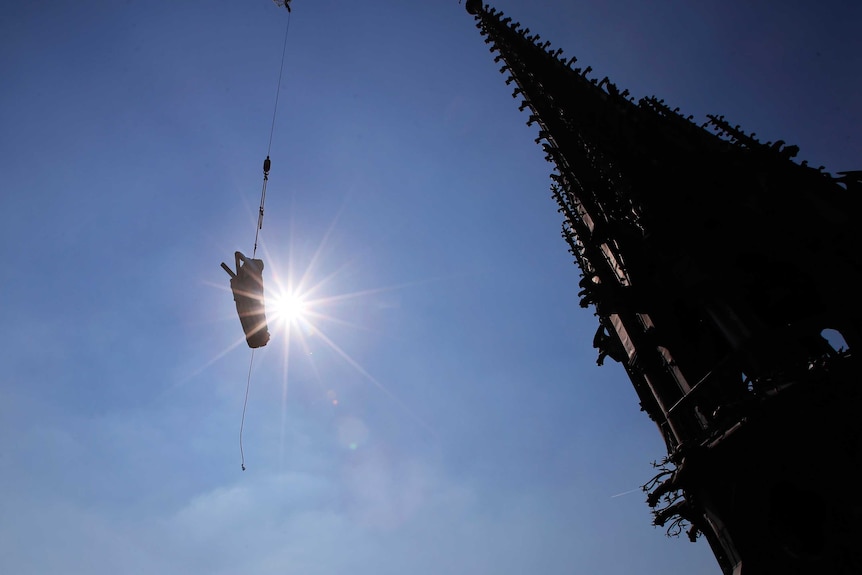 The religious statue representing St. Andrew perched atop Paris' Notre Dame Cathedral descends.
