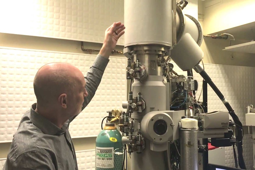 A man gestures at a scanning electron microscope.