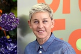 A headshot of talk show host Ellen DeGeneres, she is smiling and wearing a blue buttoned up shirt.