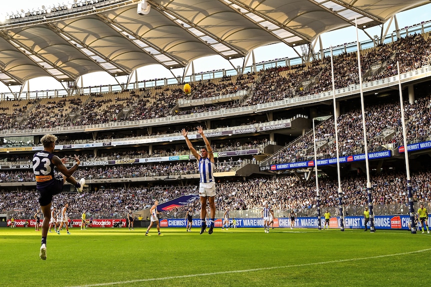 A Fremantle AFL player watches the ball sail towards the goals after taking a set shot as a Kangaroos defender stands the mark.