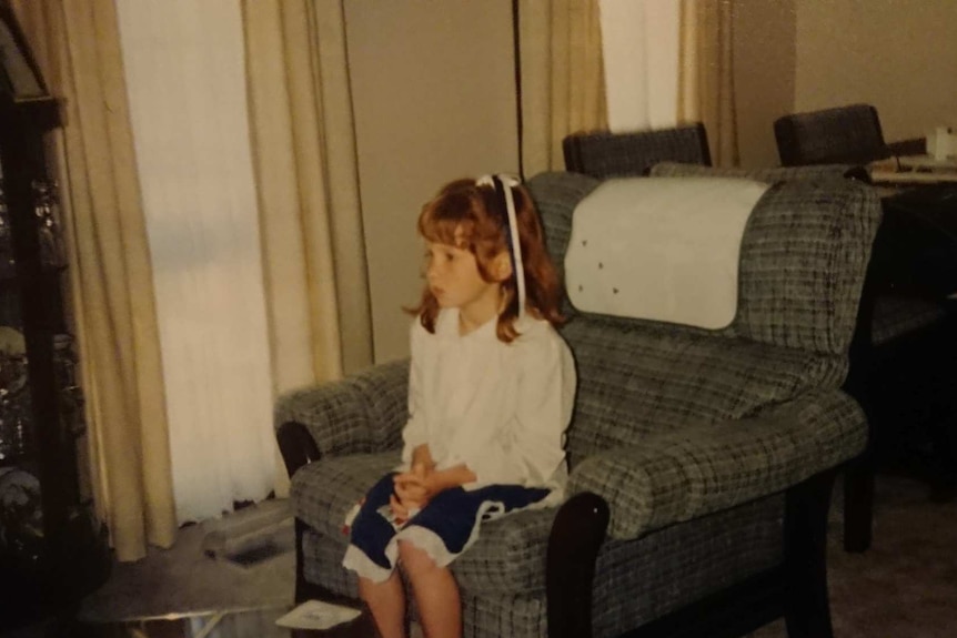 A young child sits alone on a lounge chair and stairs straight ahead