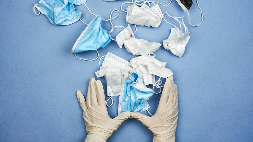 A person wearing medical gloves throws away used face masks.