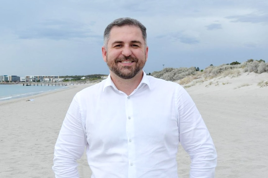 A man in a business shirt stands on a beach.