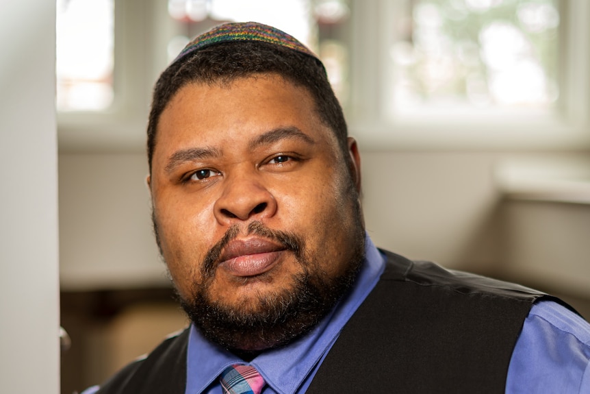 An African-American man dressed formally with a short beard, wears the Jewish skull-cap and looks directly into the camera.