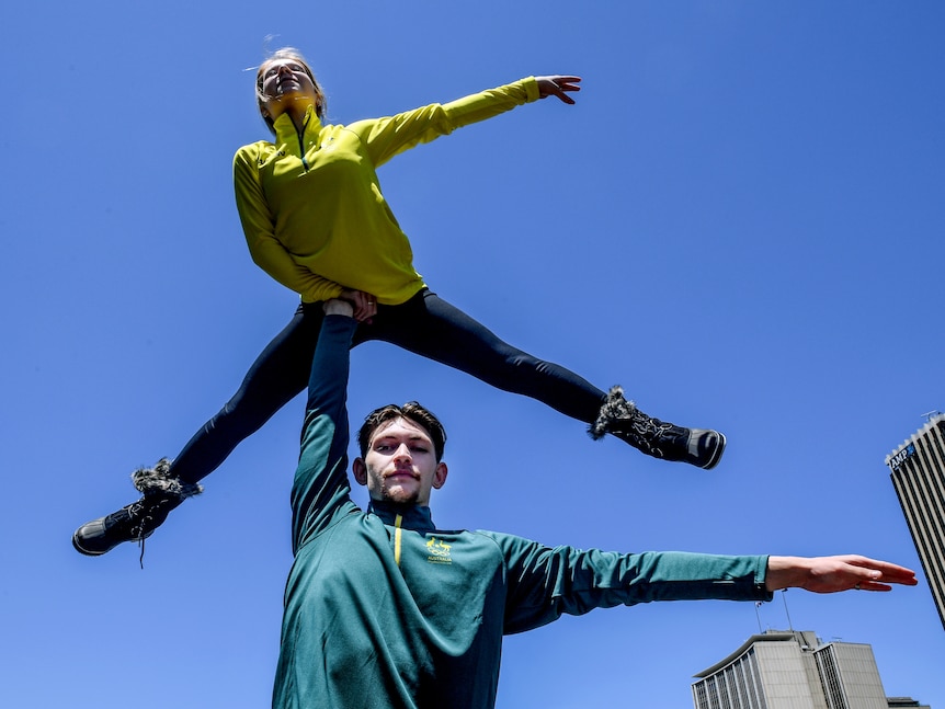 A male ice skater wearing a green Australian Olympic top lifts a female skater in a gold top above his head.