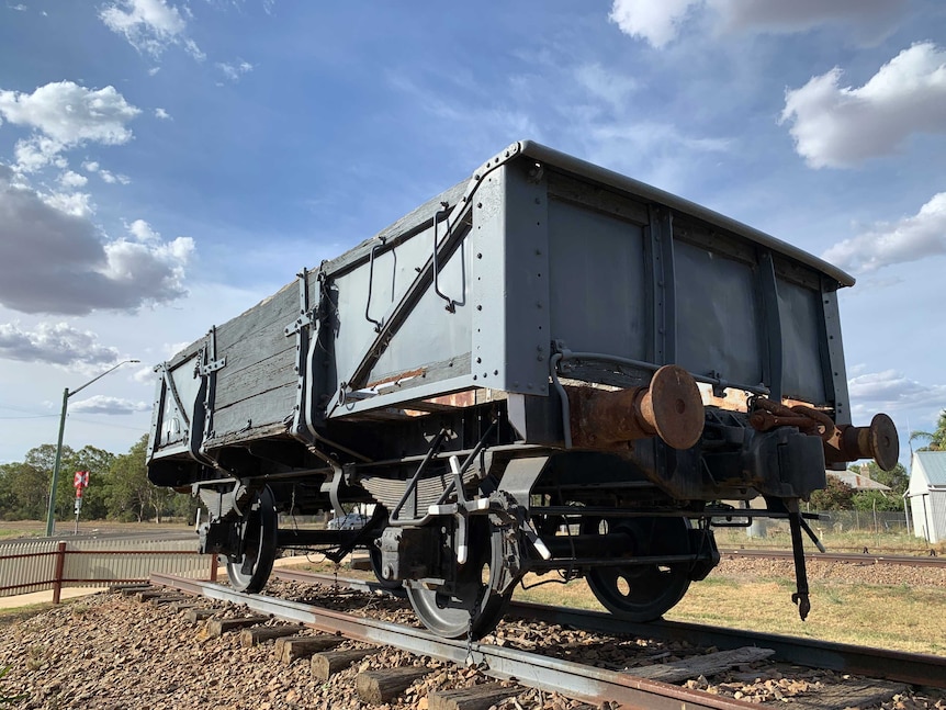 An old train goods carriage on display on old tracks, displayed behind a fence in a country town.