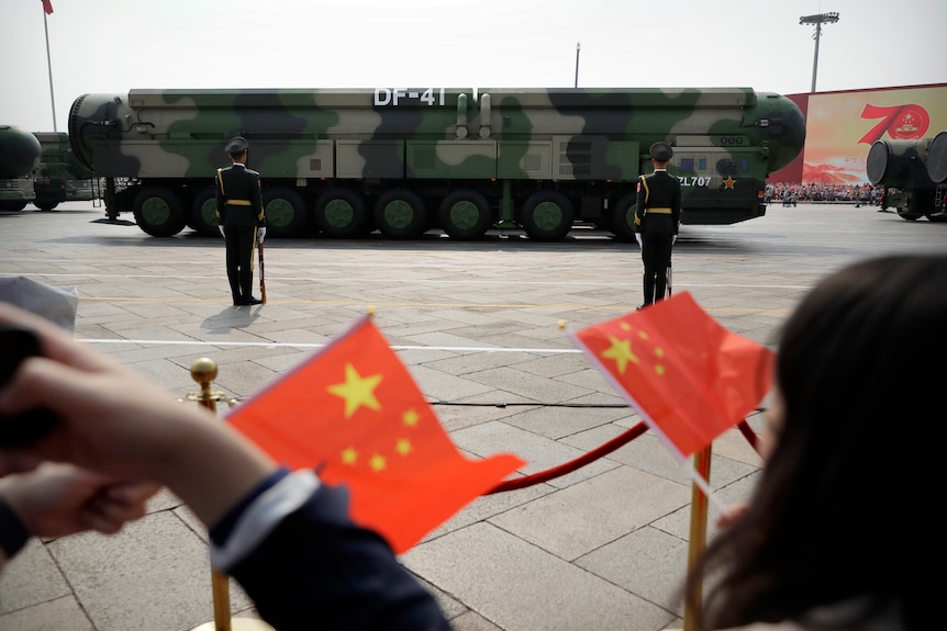 Spectators wave Chinese flags as military vehicles carrying DF-41 ballistic missiles roll during a parade.