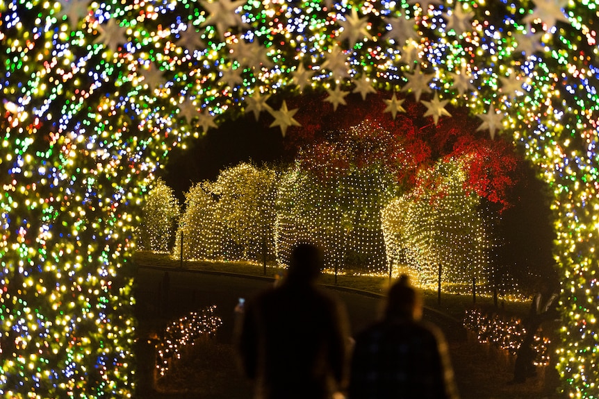 Visitors walk through a light tunnel with yellow lights and stars in California