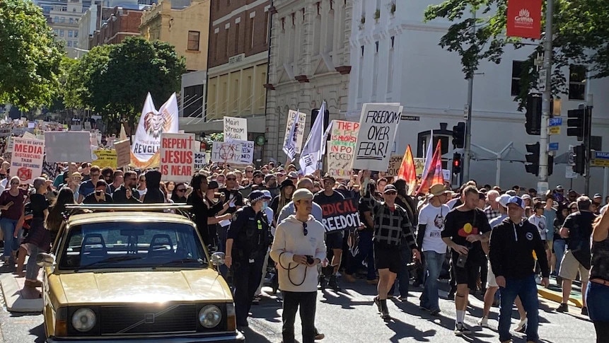 A crowd of protestors walking down a street in Brisbane. Signs include "Freedom over fear" and "Repent Jesus is Near")