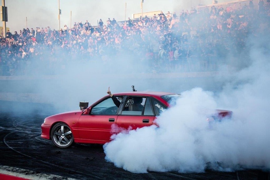 A red car does a skid in front of a large crowd