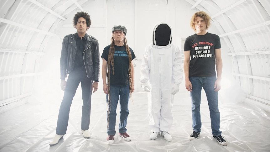 Punk group OFF! standing in a white tunnel looking into the camera. One of them dressed in a spacesuit. 