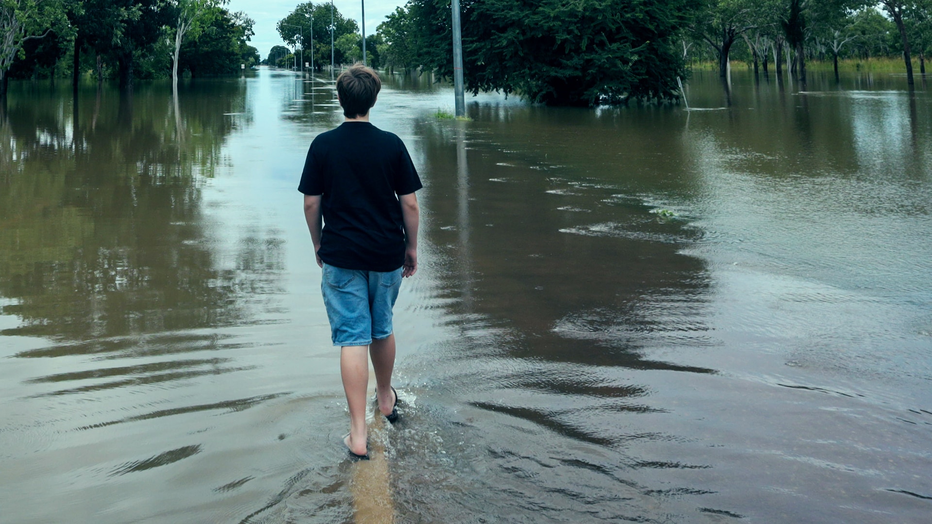 A young person walks away from camera down the middle of a flooded road.