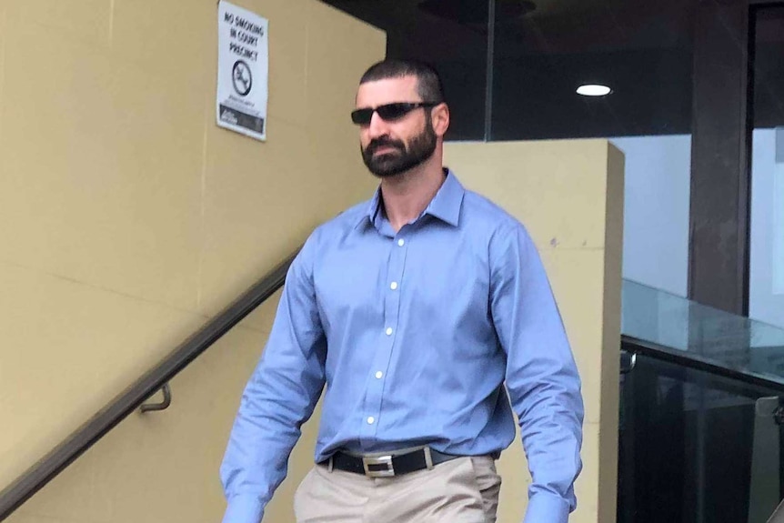 A man witha  black beard and black sunglasses leaves a court house.