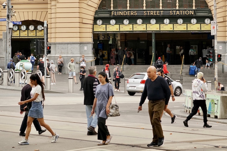Pedestrians walk past the Flinders and Swanston streets intersection on an overcast day.
