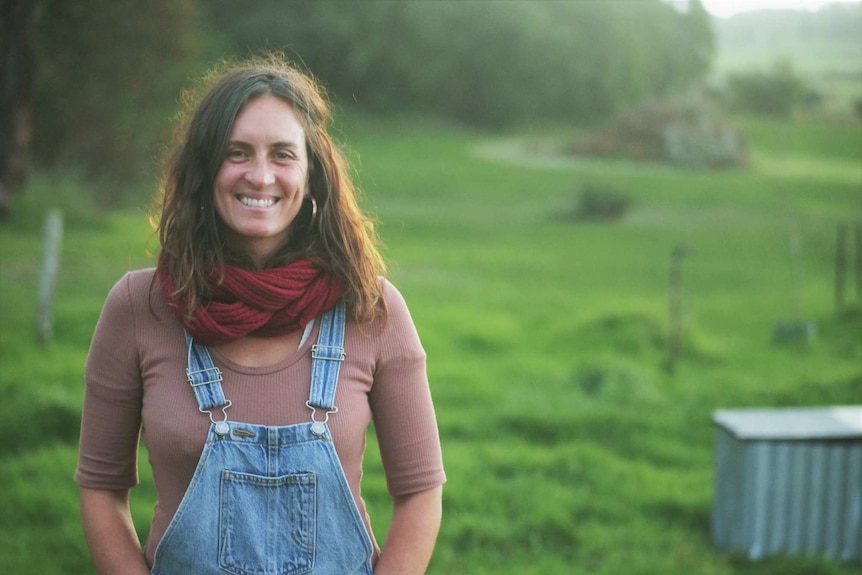 A woman wearing denim dungarees standing in a lush green paddock.