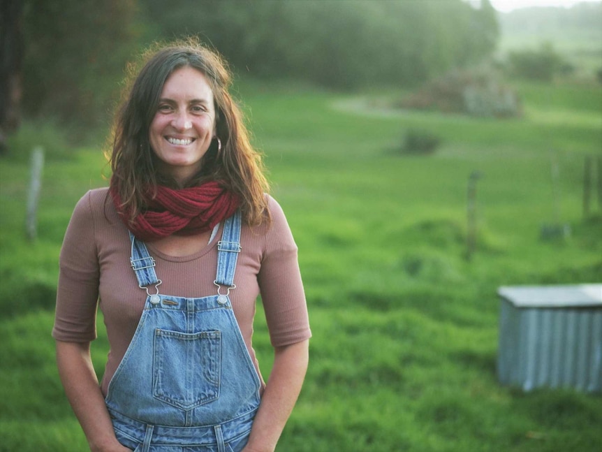 A woman wearing denim dungarees standing in a lush green paddock.