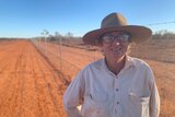 A woman stands by a long tall fence in the red dust of western Queensland