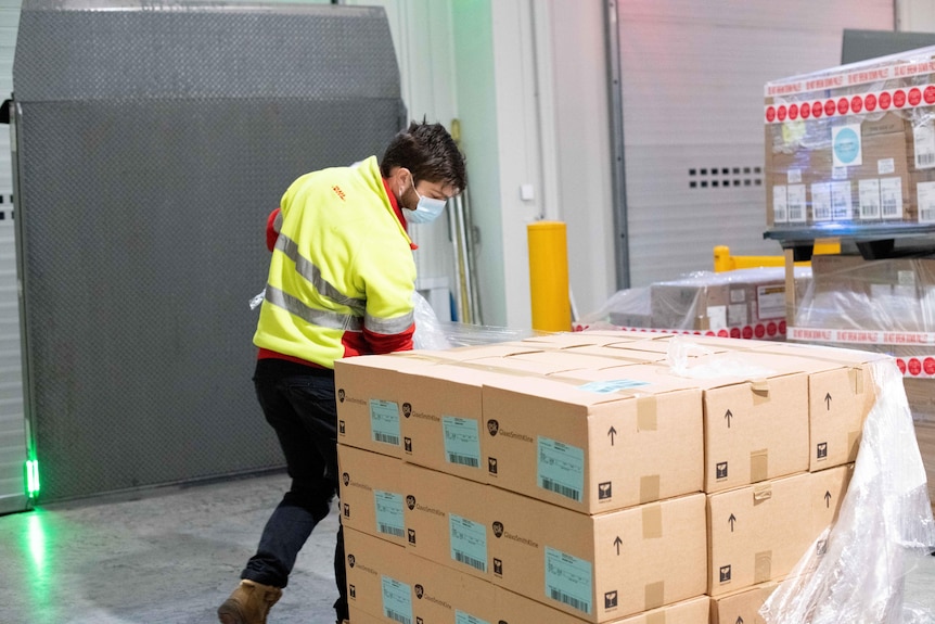 A man in a high-vis vest looking at pallet stacked with boxes.