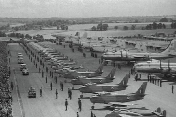Black and white photo of an airstrip full of all types of planes and military personnel at attention