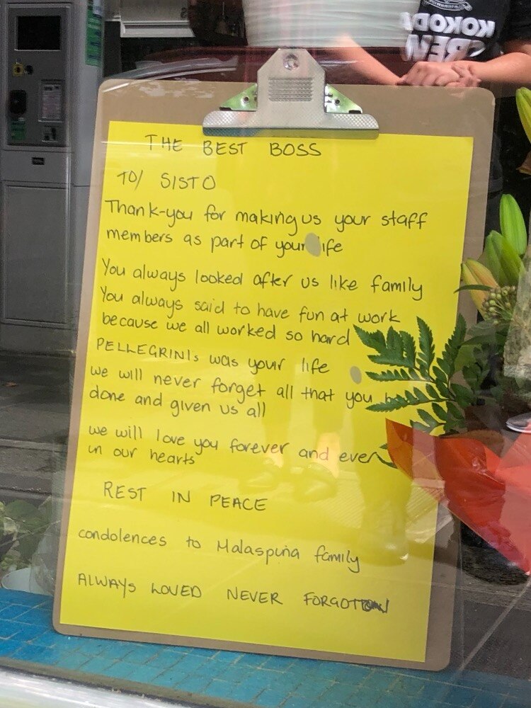 A clipboard in a window with writing on a yellow piece of paper.