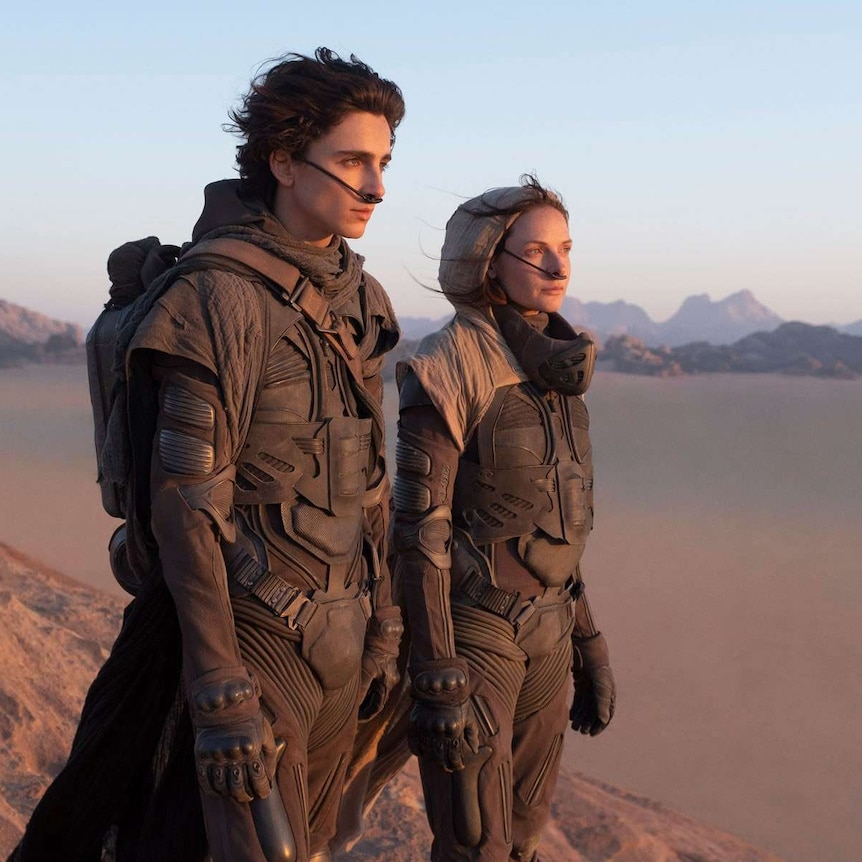 Two actors dressed in futuristic armour in the foreground of a vast desert, staring into the distance.
