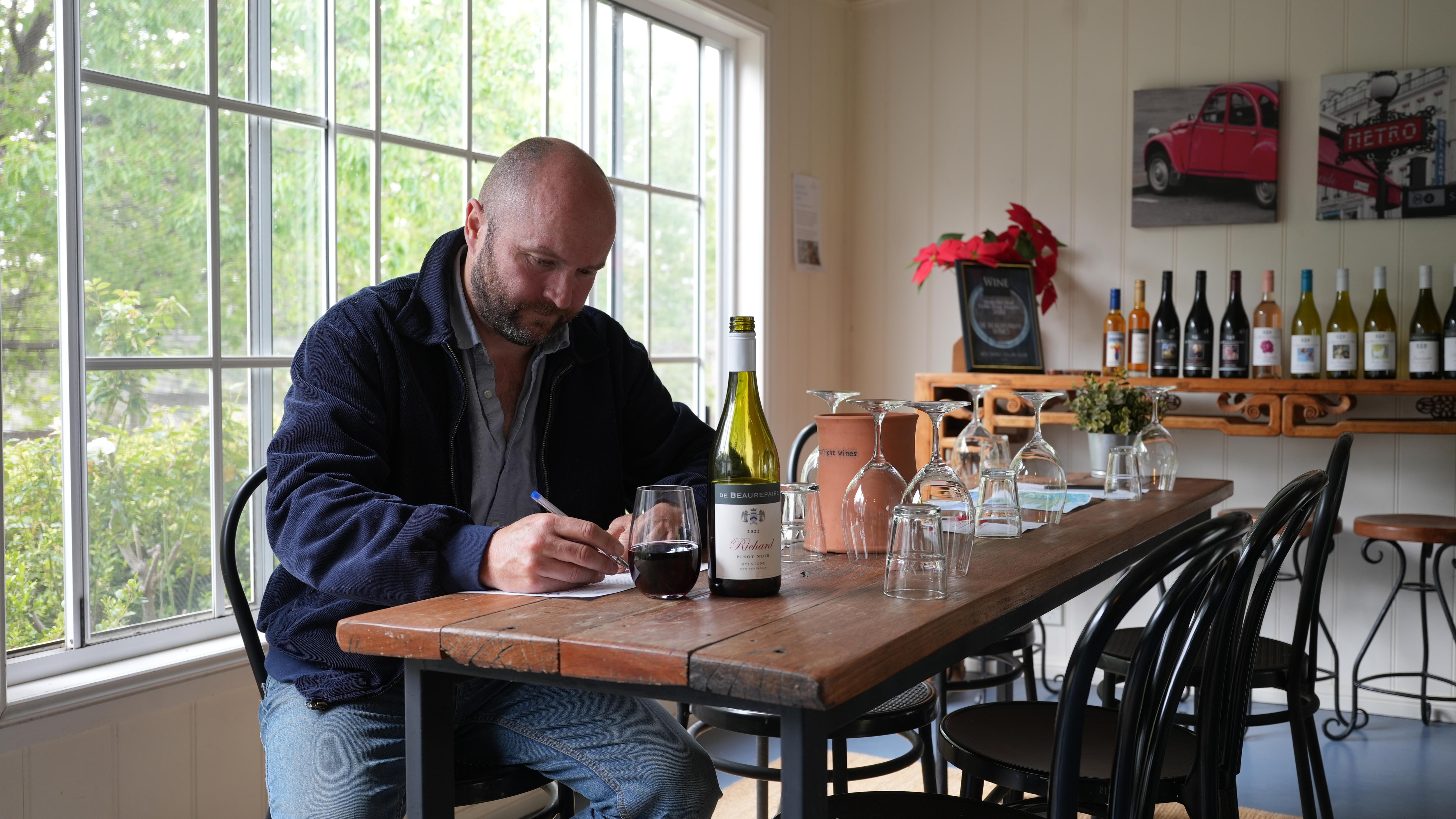 A man writing while sitting next to a bottle of wine