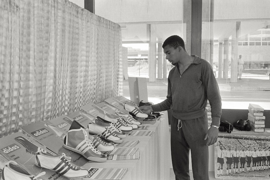 An athlete walks around looking at old Adidas shoes.